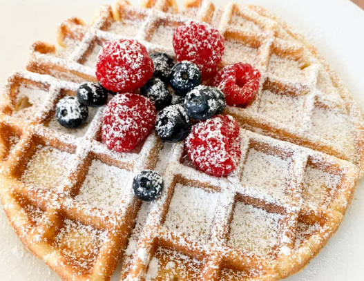 A golden-brown waffle topped with fresh raspberries and blueberries, lightly dusted with powdered sugar.