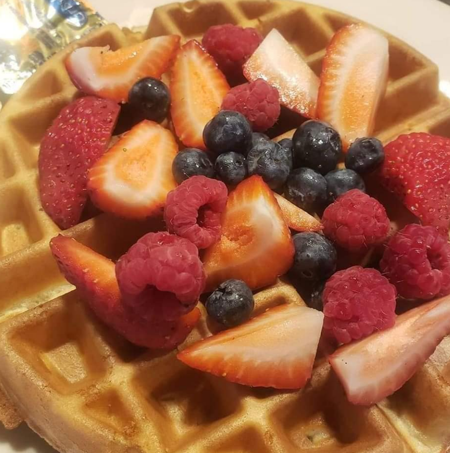 A golden-brown waffle topped with fresh sliced strawberries, blueberries, and raspberries.