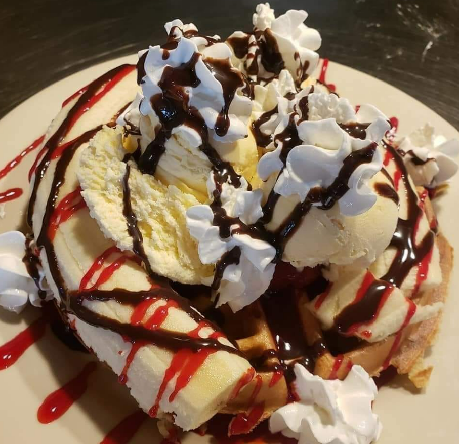 A waffle topped with vanilla ice cream, banana slices, whipped cream, and drizzles of chocolate and strawberry syrup.