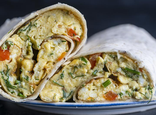 Two halves of a breakfast burrito filled with scrambled eggs, herbs, and diced tomatoes on a plate.
