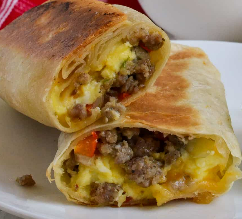 A sliced breakfast burrito filled with crumbled sausage, scrambled eggs, and diced peppers on a white plate.