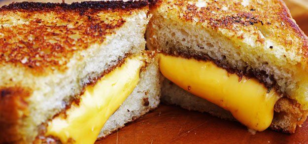 A close-up of a halved grilled cheese sandwich on toasted bread with melted yellow cheese on a wooden surface.