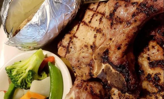 A grilled T-bone steak with a foil-wrapped baked potato and a side of mixed vegetables, including broccoli.