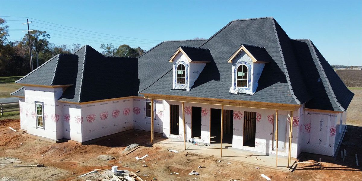 Partially built two-story house with white siding, dark roof, and front porch under construction