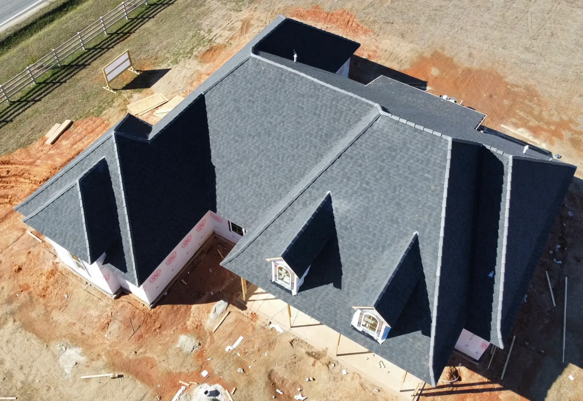 Aerial view of a dark gray house foundation with roof framing on a dirt lot during construction