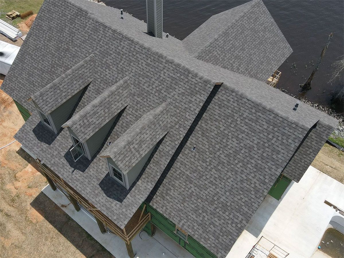 Aerial view of a gray shingled house roof with multiple dormer windows and a driveway beside it
