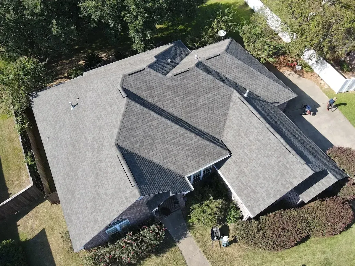 Aerial view of a house with a gray shingle roof and surrounding yard with trees.