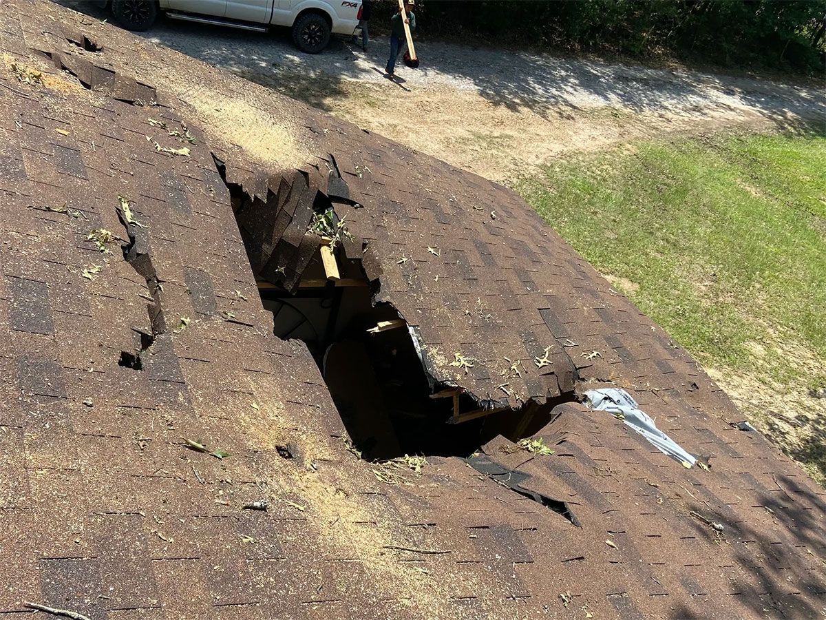 Collapsed asphalt roof with a large hole exposing the structure beneath outdoors.