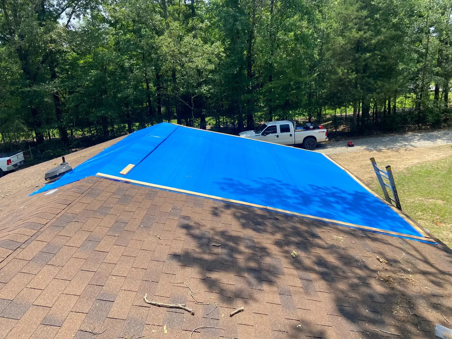 Blue tarp covering a dirt mound at a wooded worksite, with a white truck in the background