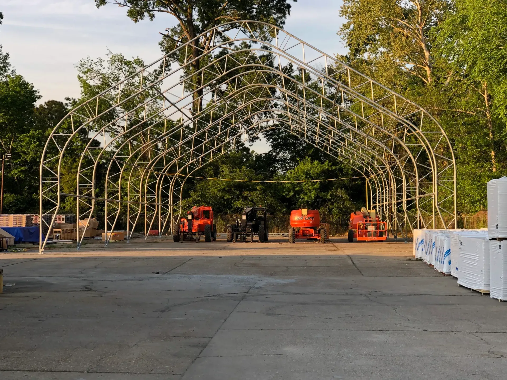 Outdoor arch of metal frames over a paved area with orange construction vehicles and white barriers on the right