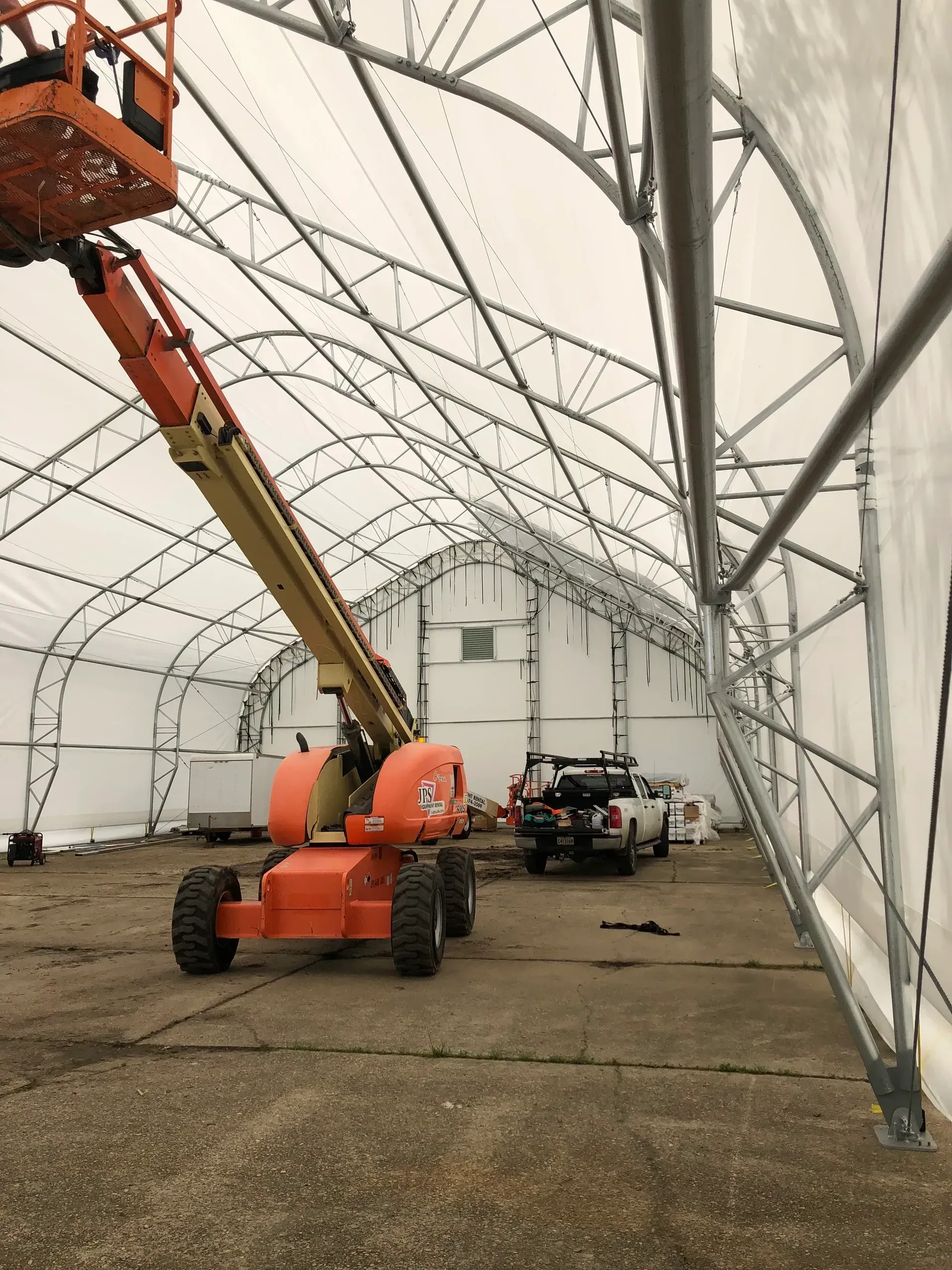 Orange boom lift inside a white tented structure with equipment on the ground.