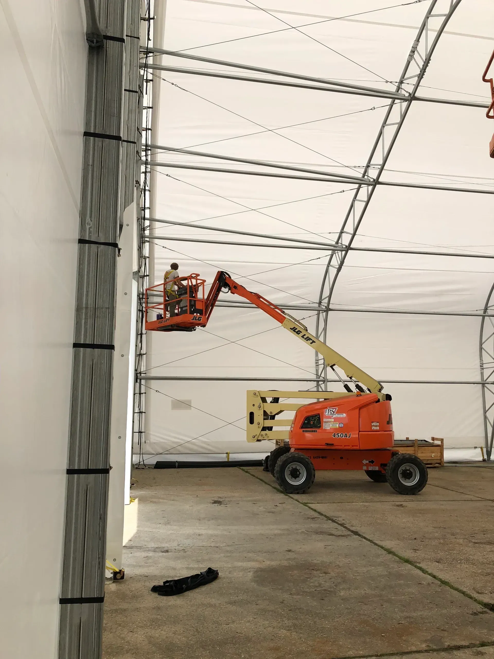 Cherry picker lifting a worker near a concrete wall inside a large white tent
