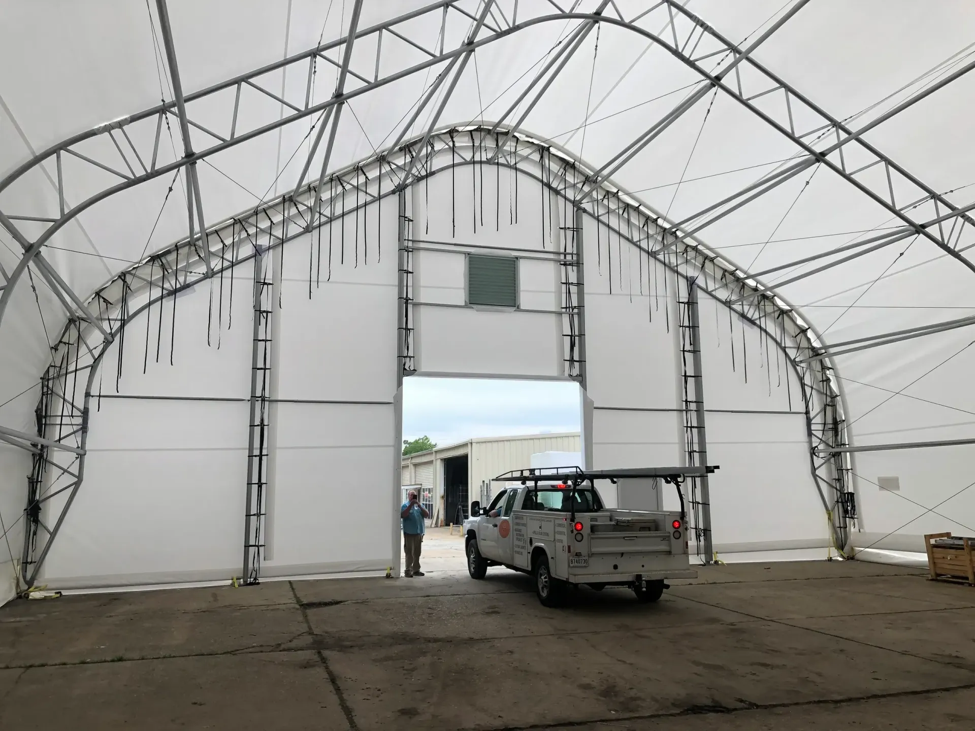 Large white tent interior with a pickup truck parked at the open entrance and two people near the doorway.