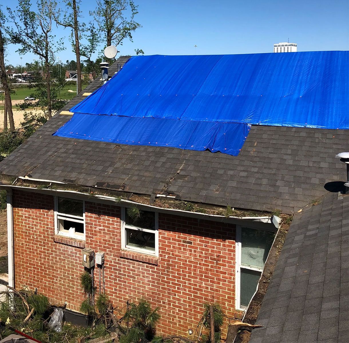 Brick house roof covered with a bright blue tarp over damaged shingles