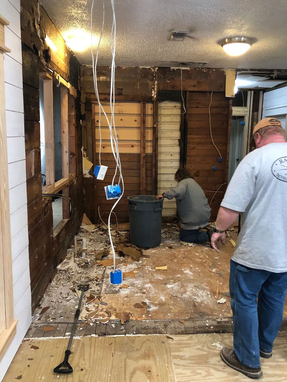 Damaged room with exposed walls, debris on floor, and two workers inspecting the space