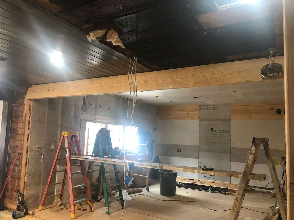 Indoor construction site with ladders, exposed beams, and workers near a bright window