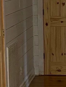 Wood-paneled hallway corner with a white wall vent and a wooden door