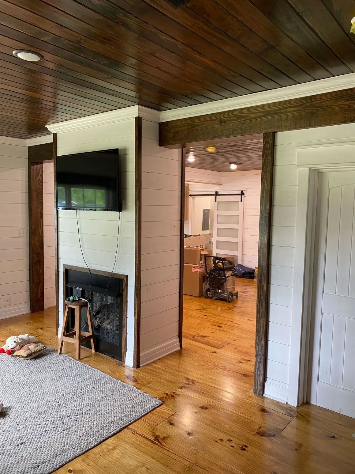 Living room with wood ceiling, fireplace, TV, and view into a bright adjoining room