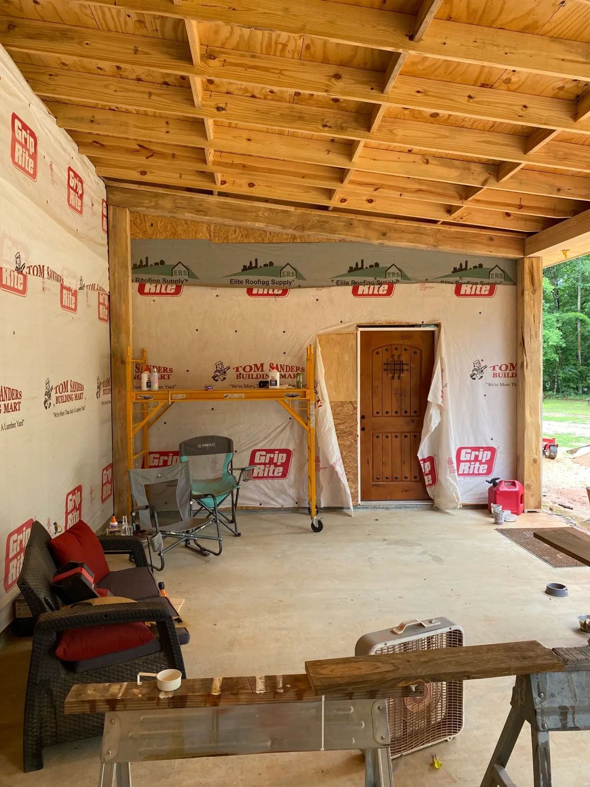Unfinished room with exposed wooden ceiling, insulated walls, a door, and scattered tools and materials.