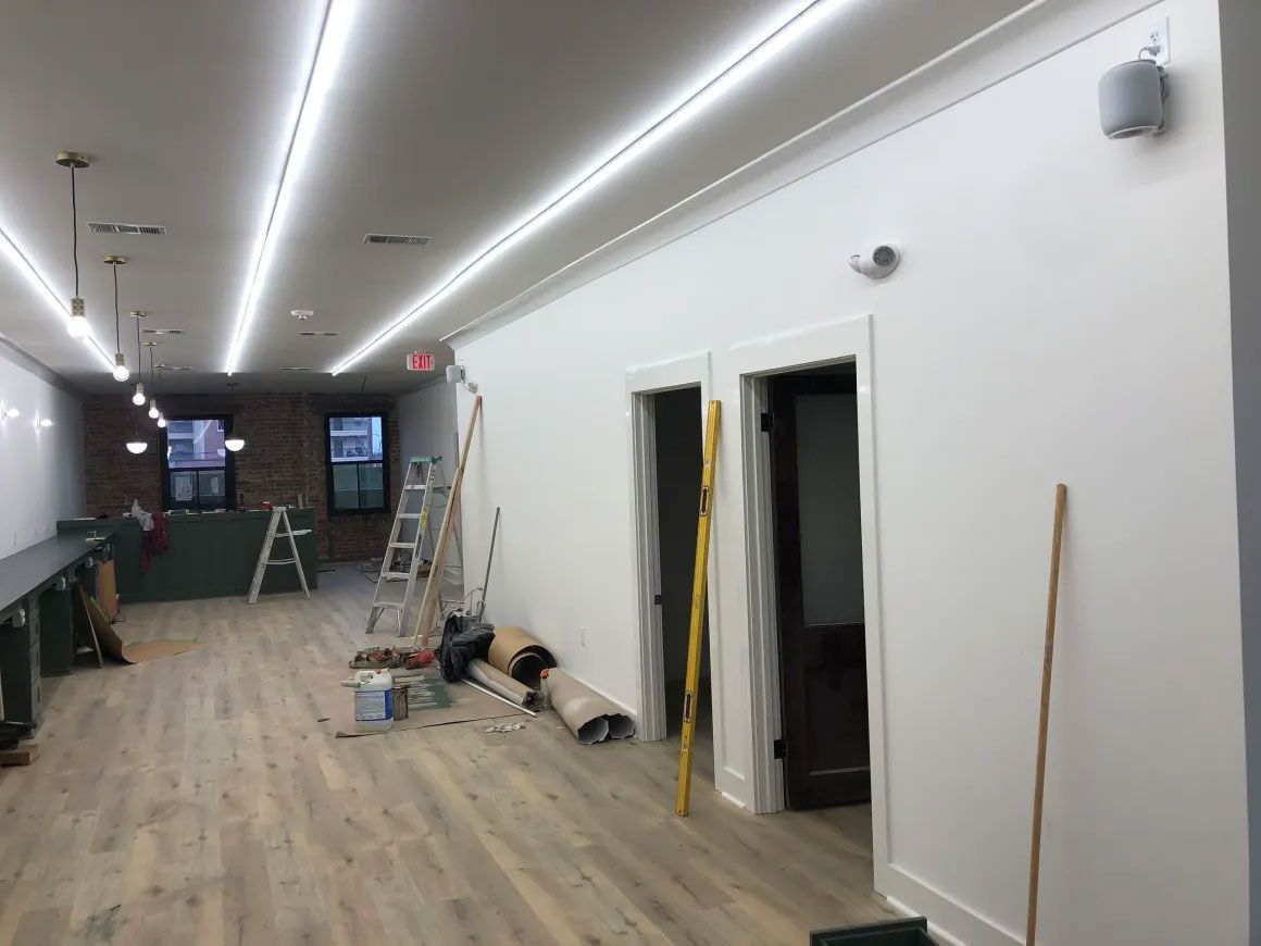Long hallway with white walls, wood floor, ladders, tools, and open doorways during renovation