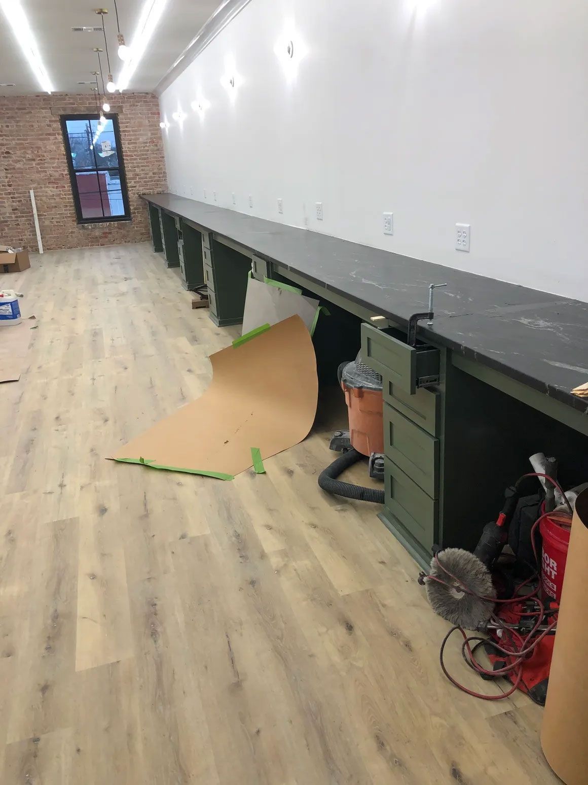Long workshop with unfinished cabinets, wood floor, and a cardboard sheet on the floor.