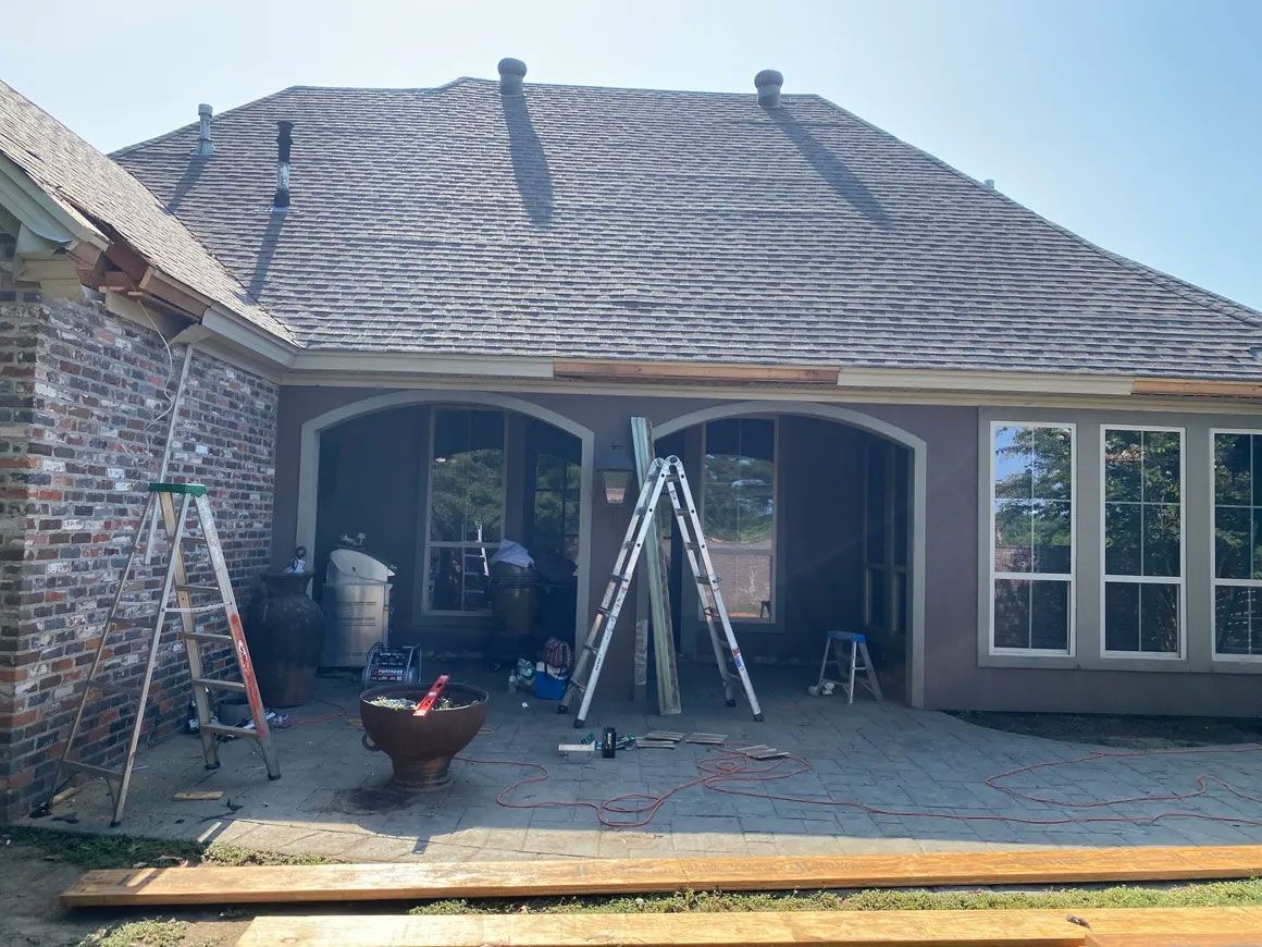 Patio with ladder and tools in front of a house roof being worked on after storm damage