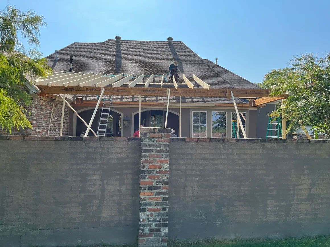 House under construction behind a brick wall, with a tiled roof and ladder under a blue sky