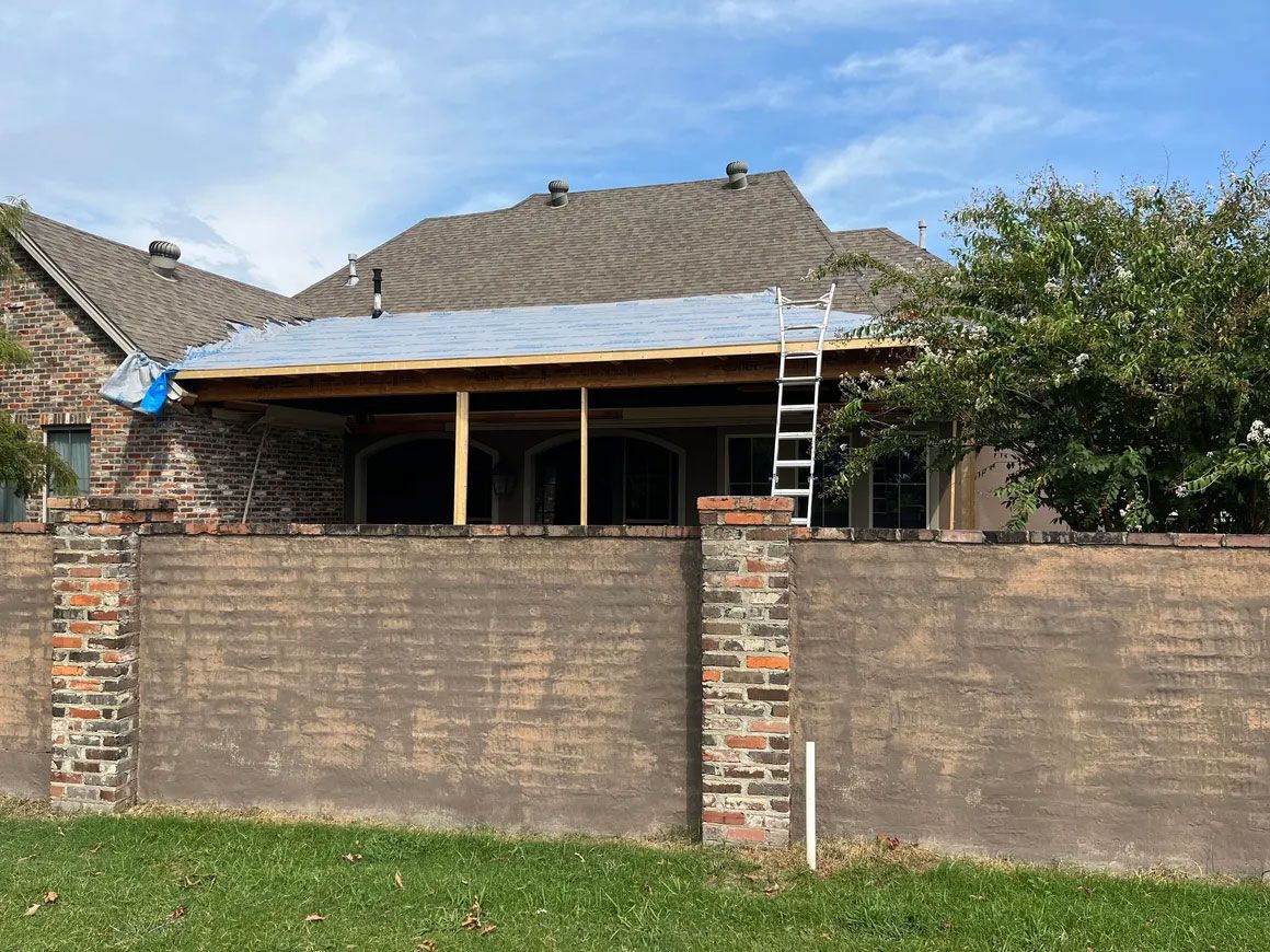 Backyard house with brick wall, exposed porch roof, and a ladder leaning against the roofline