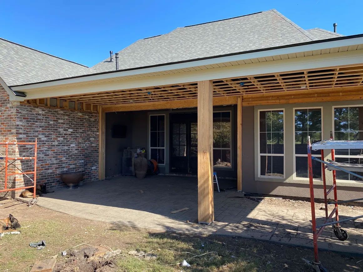 Backyard patio under construction with brick walls, wooden posts, and partially finished roof trim