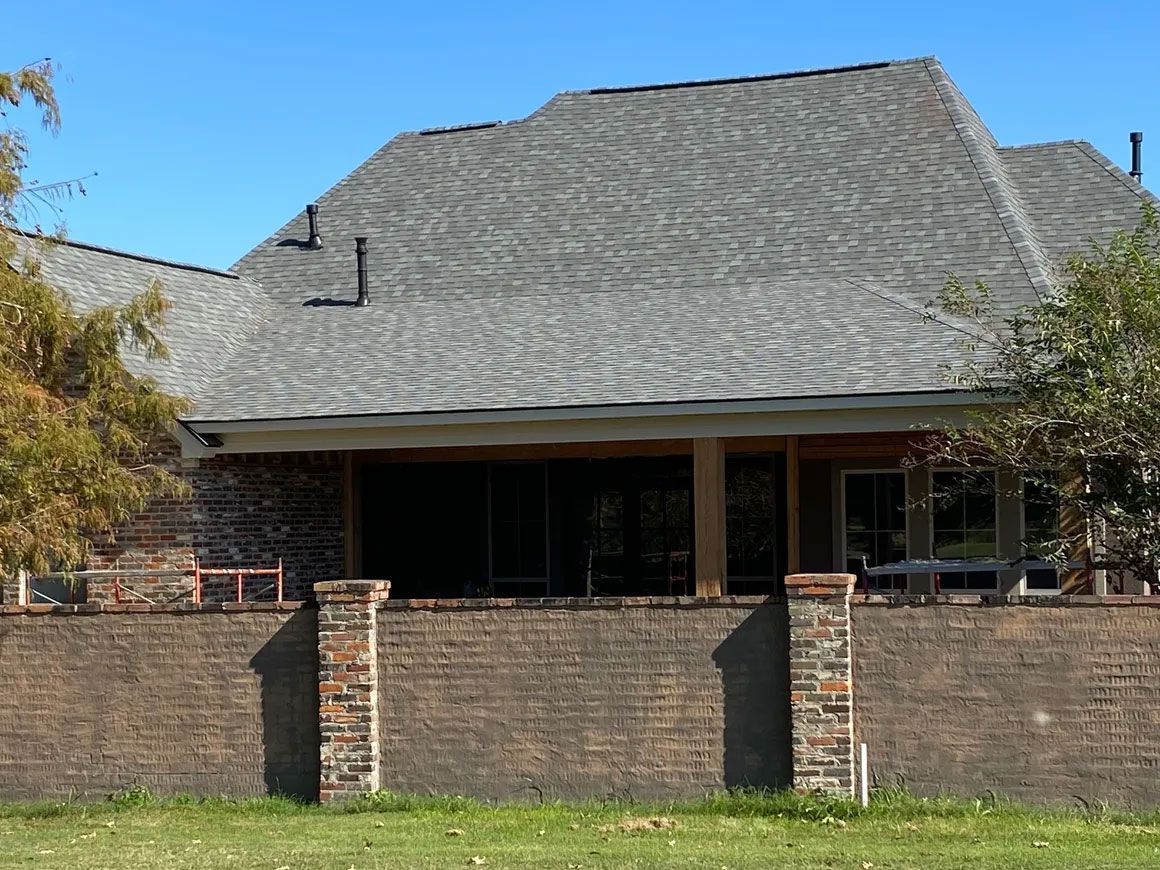 Brick house with a large gray roof and a front porch behind a low brick wall.