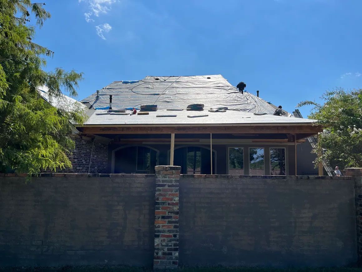 Partially demolished house behind a tall brick wall under a bright blue sky