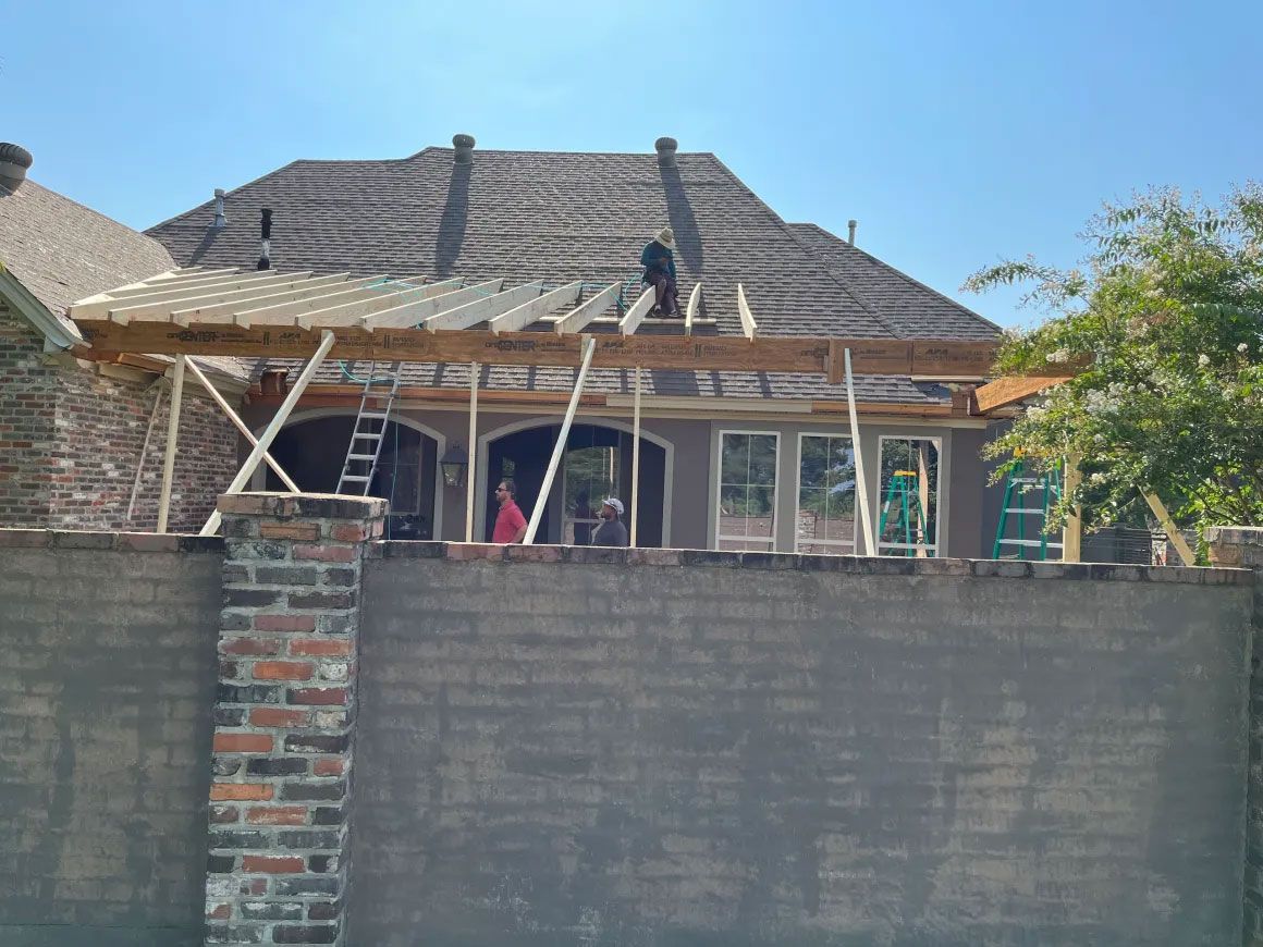 Damaged house roof under repair behind a brick wall, with workers on the roof and scaffolding in front.