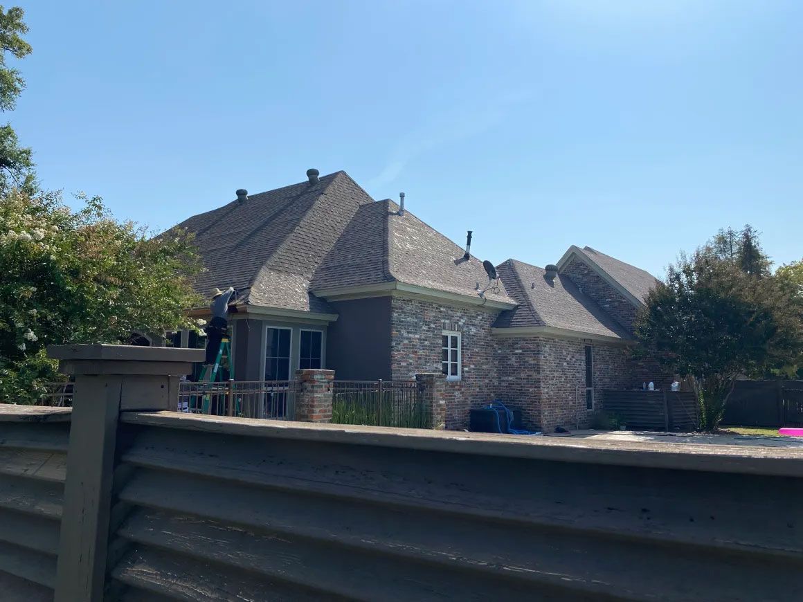 Stone house with a dark roof behind a wooden fence under a clear blue sky
