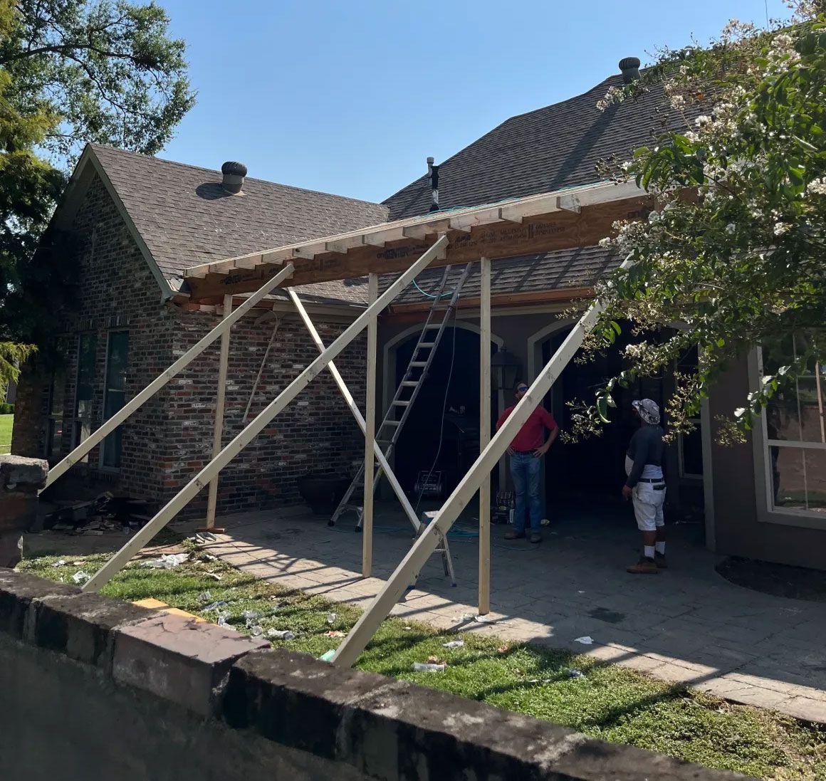 Wooden scaffolding beside a stone house, with people working under the roof overhang.