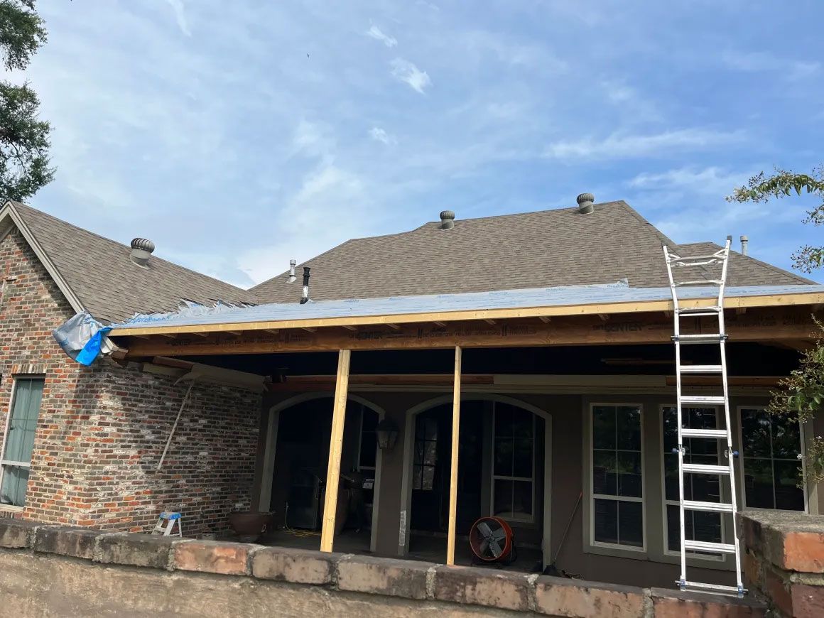 Partially built porch with wooden supports and ladder beside a brick house under a blue sky