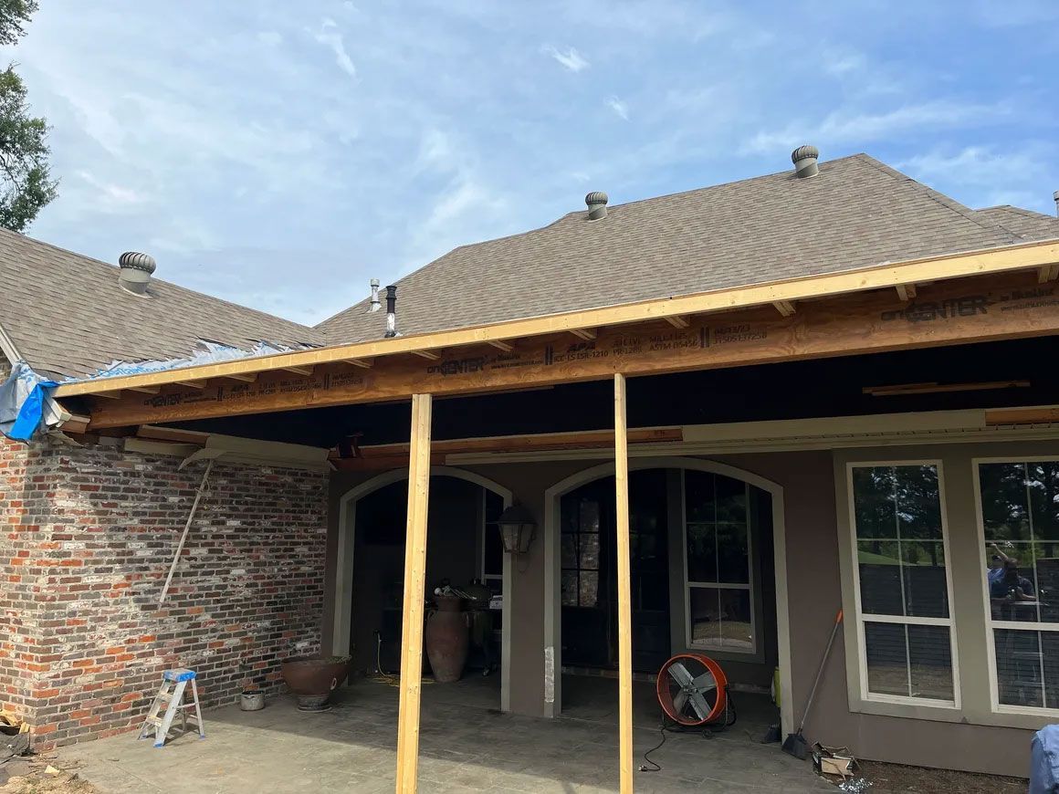 Patio with exposed roof framing and support posts in front of a house, partly under construction