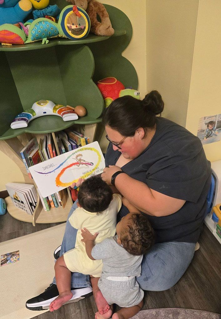 A person reads a book to two children in a colorful playroom.
