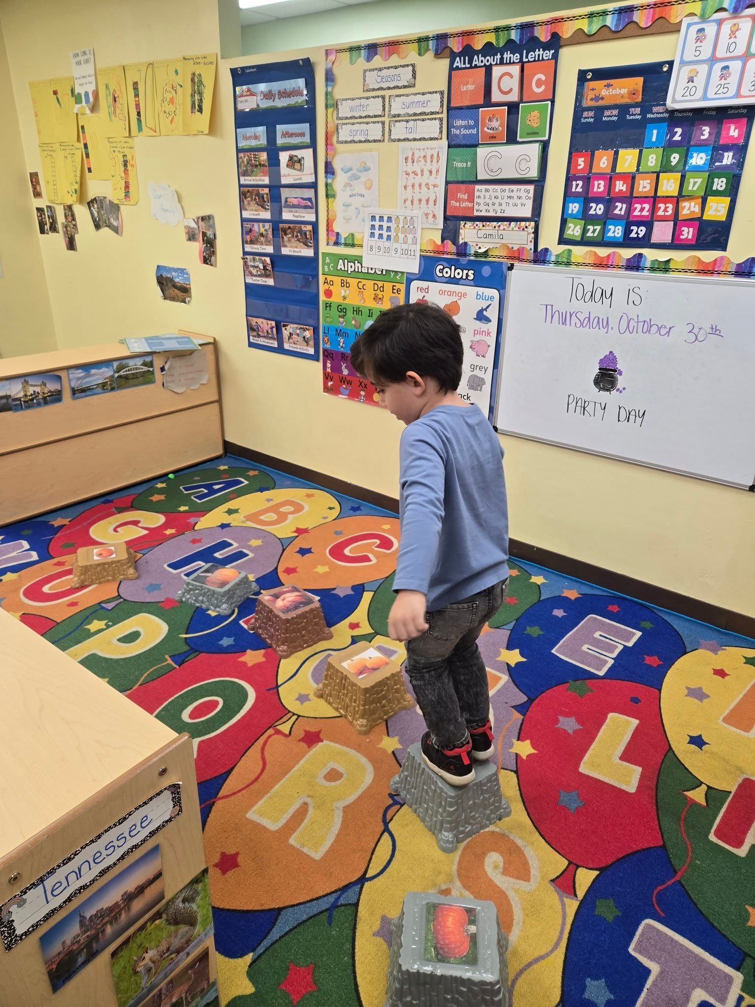 A child walks across blocks on a colorful alphabet rug in a classroom.