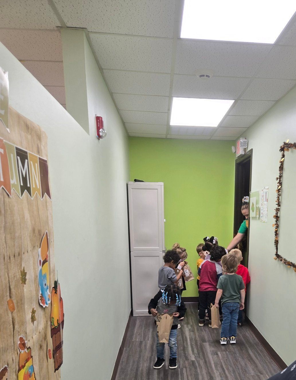 Children in a hallway, lined up by a door.