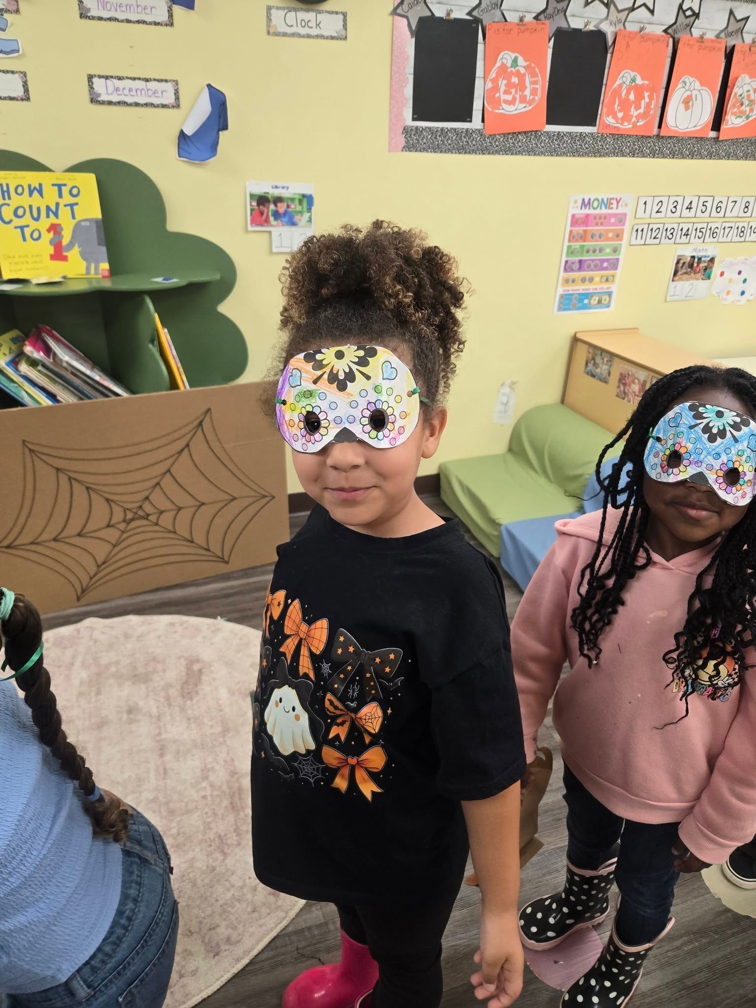 Two children wearing decorated masks and Halloween shirts in a classroom.