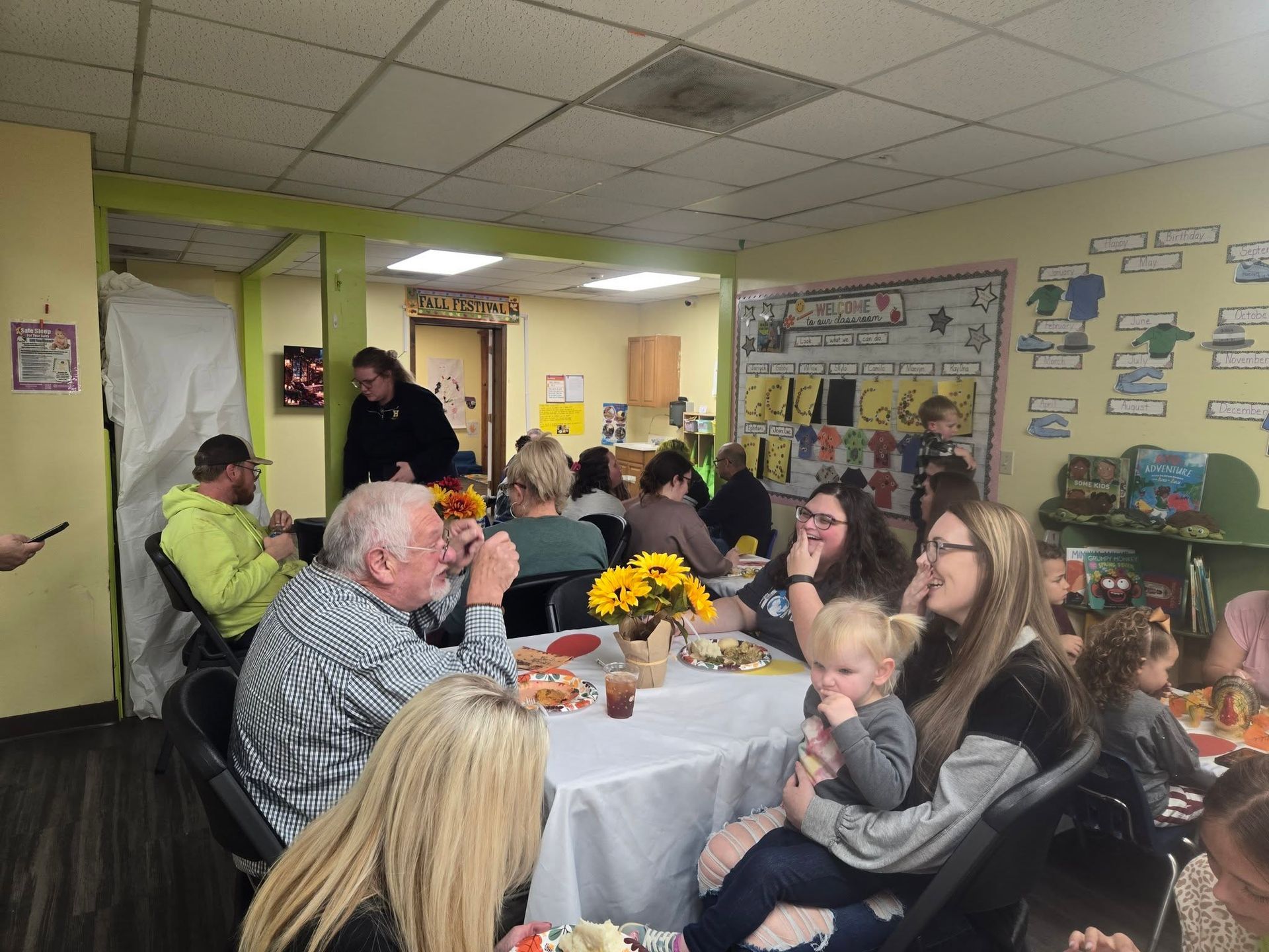 People seated around a table, a gathering inside a brightly lit room.