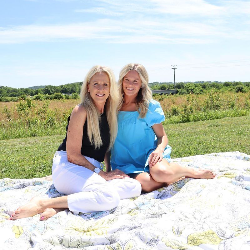 Two women are sitting on a blanket in a field