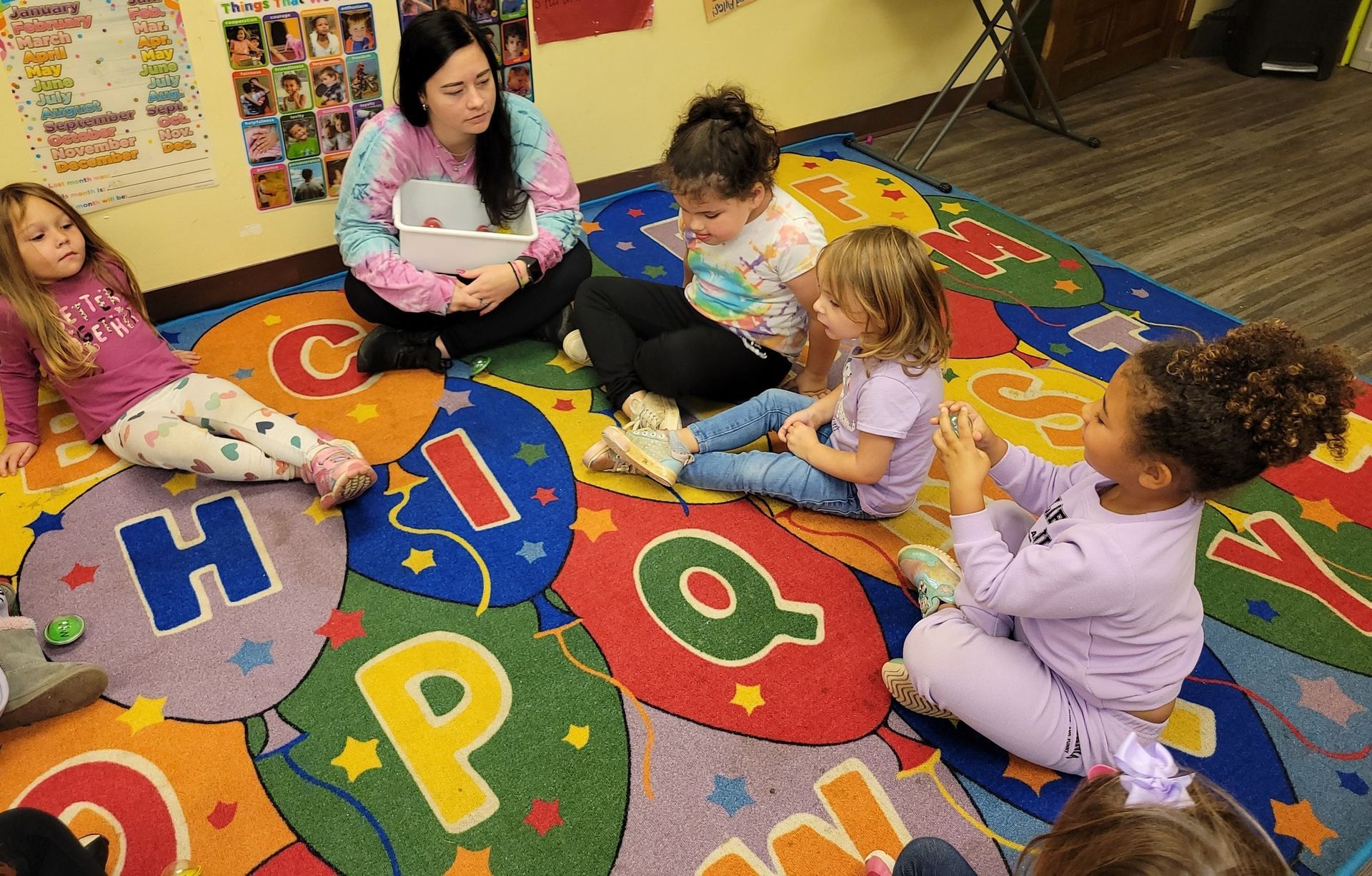 A group of young girls are sitting on a colorful rug on the floor.
