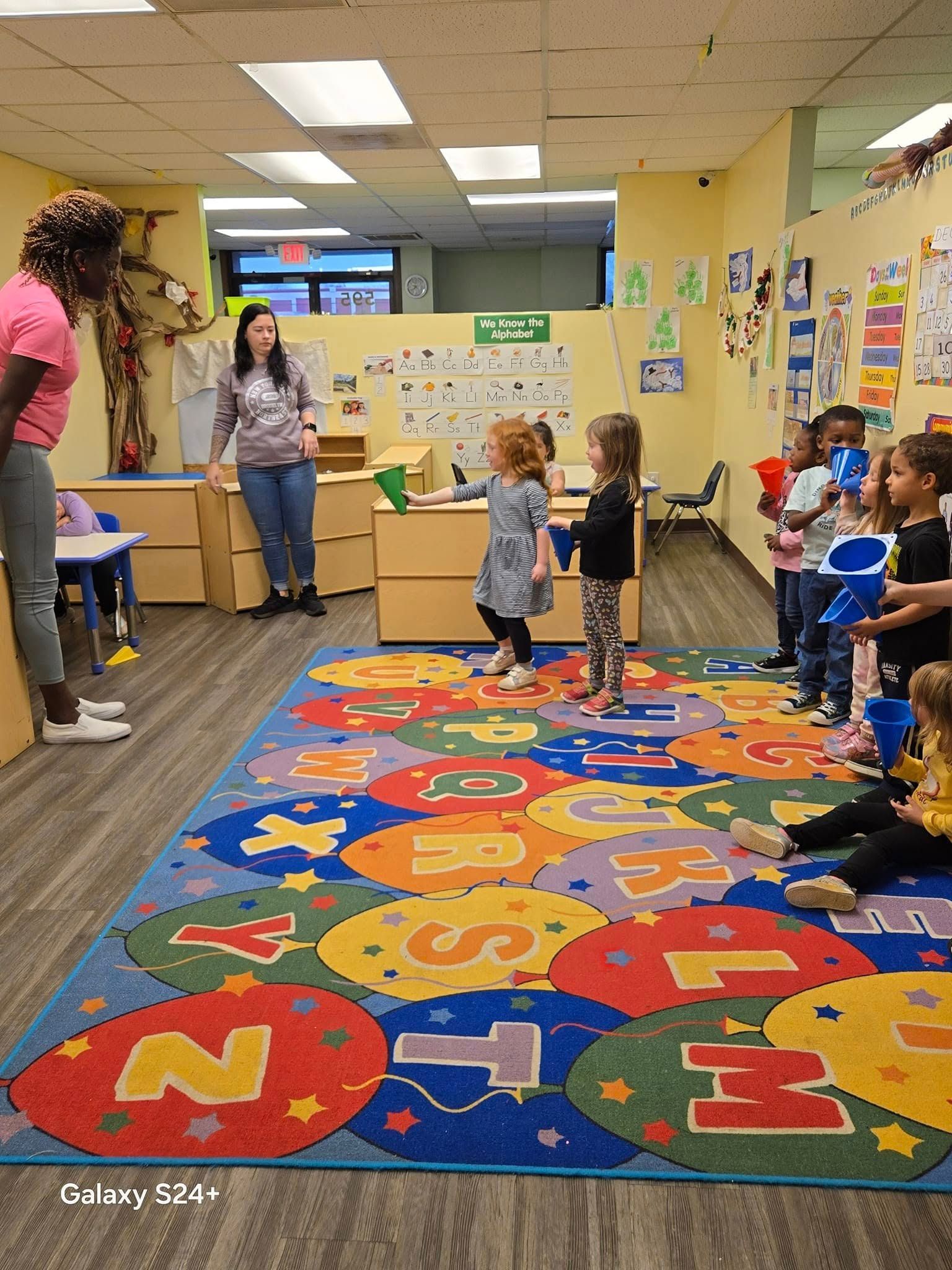 A group of children are playing in a classroom with a colorful rug.