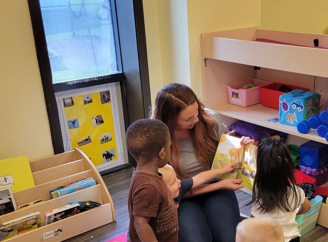 A woman is sitting on the floor reading a book to two children.