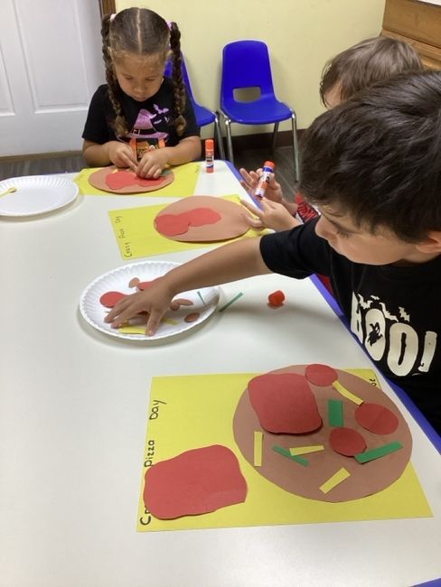 Children at a table making pizza crafts with paper and glue.