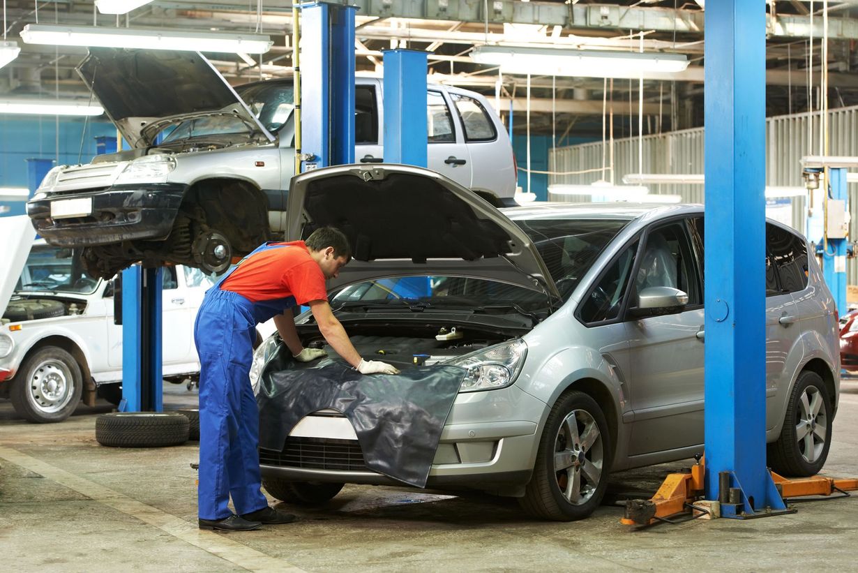 Mechanic in blue coveralls working on silver car in auto repair shop, other cars on lifts.