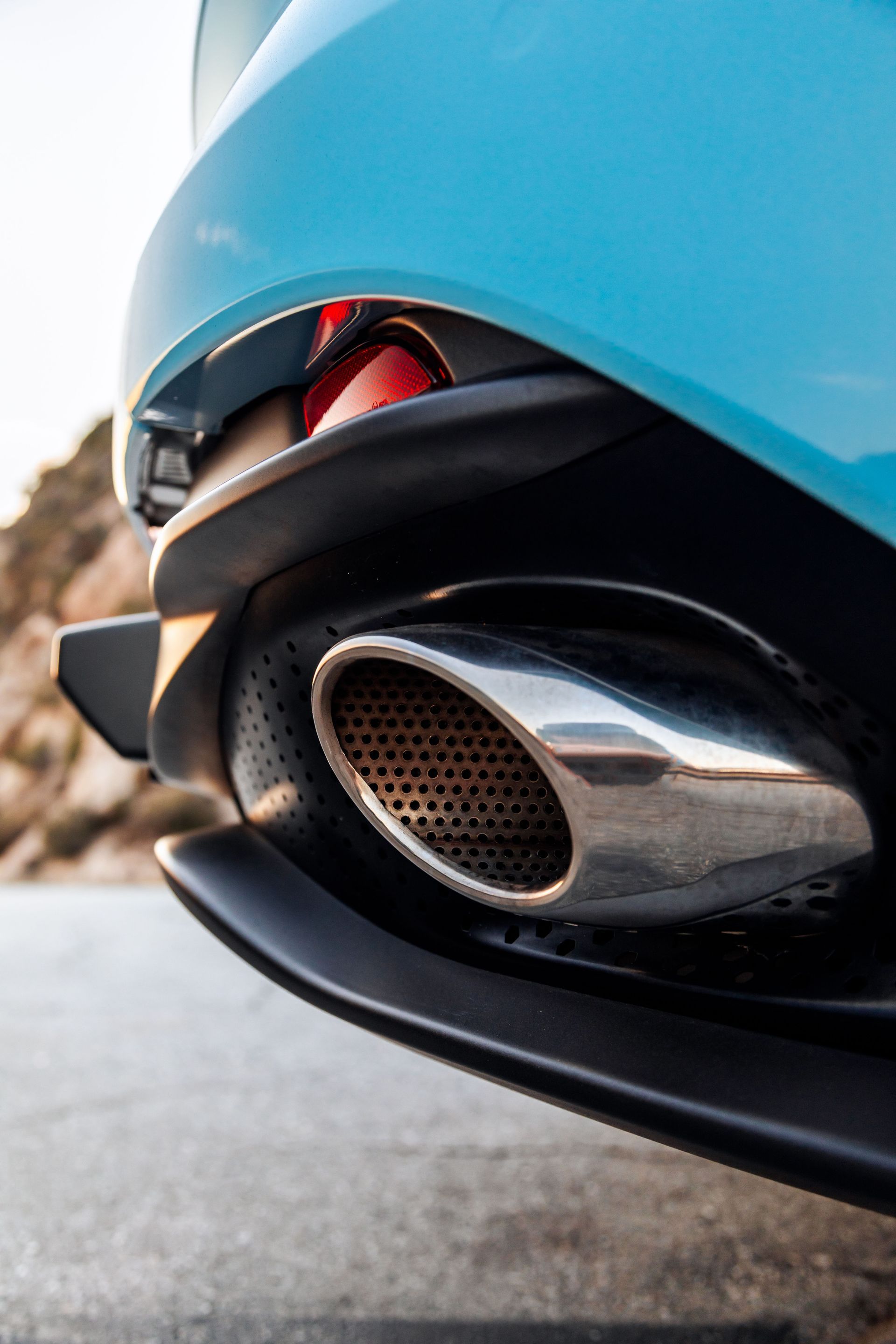 Chrome exhaust pipe on a blue sports car, with a black trim and red taillight.