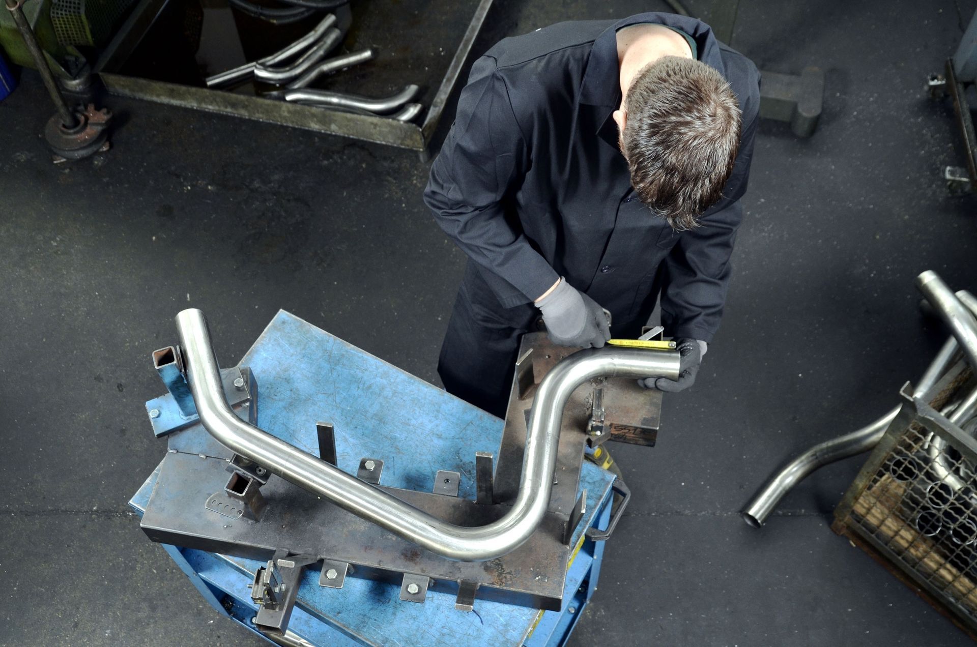 Mechanic working on a curved metal pipe in a workshop.