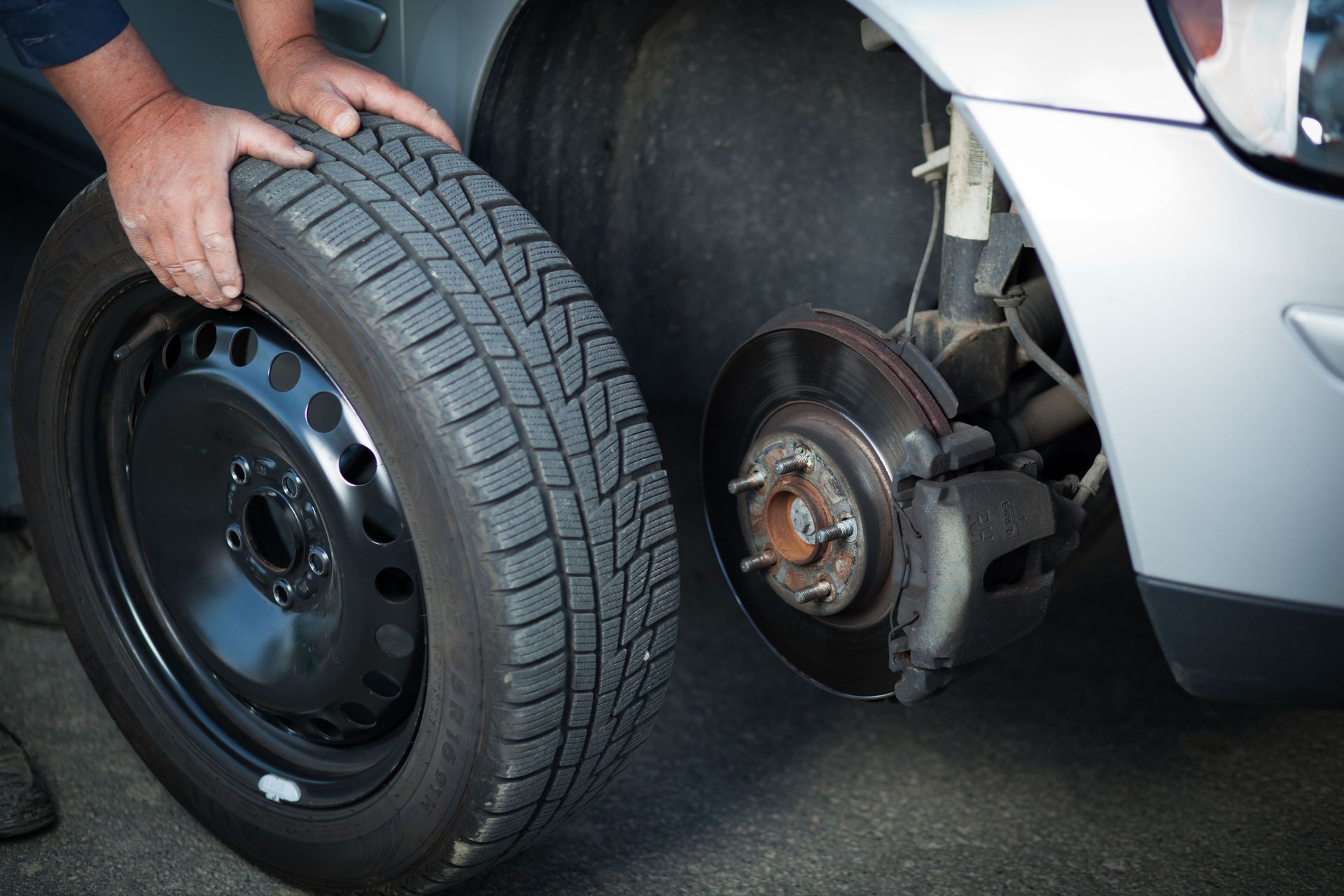 Person holding a tire next to a car with the wheel removed, showing the brake assembly.